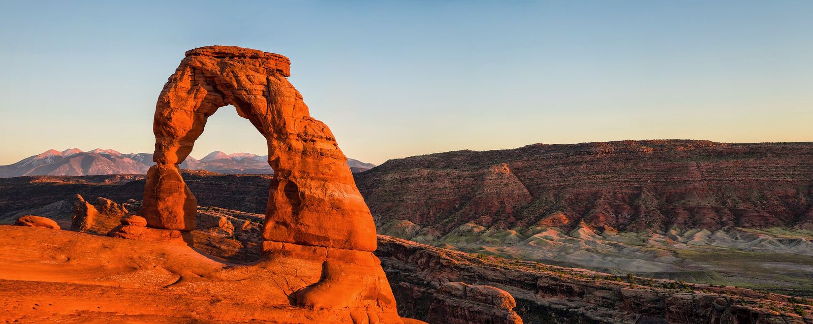 Delicate Arch glowing orange at sunset above the red-rock canyons of Arches National Park, Utah.